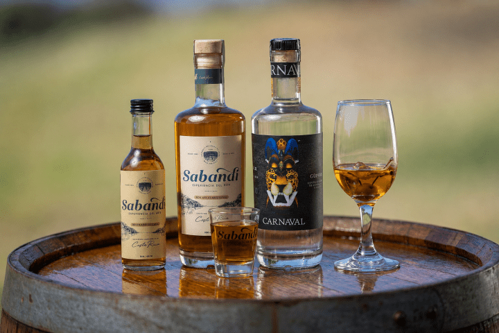 Three liquor bottles and a glass on a wooden barrel.