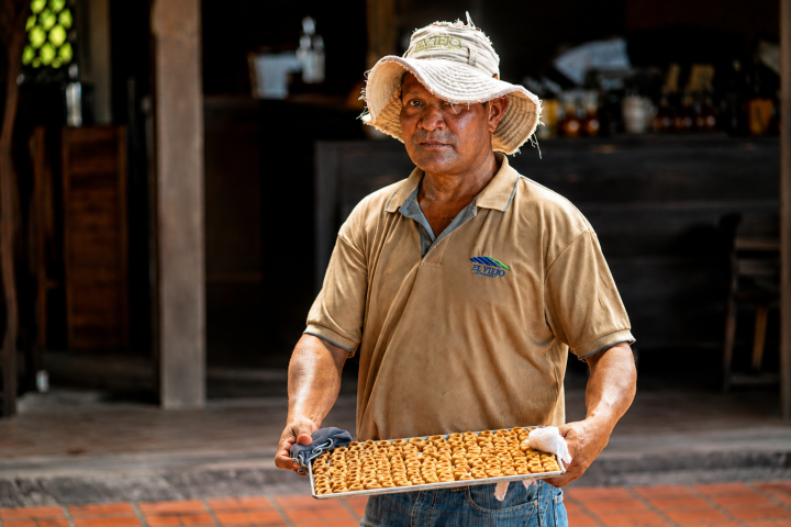 Man in hat holding tray of pastries in a rustic setting.