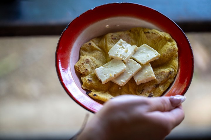 Hand holding a plate with flatbread and cheese pieces.