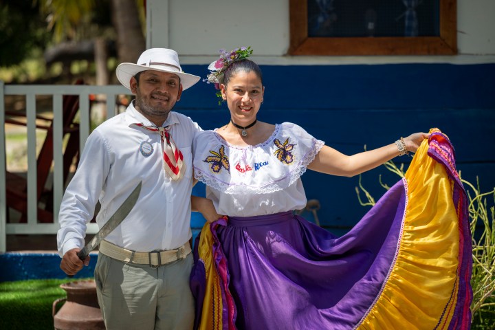 Man and woman in traditional costumes, smiling outdoors.