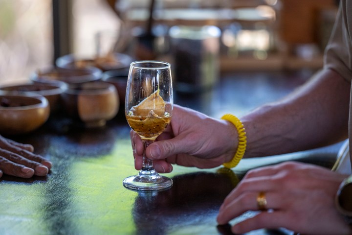 Hand holding a glass with a yellow drink on a table with wooden bowls.