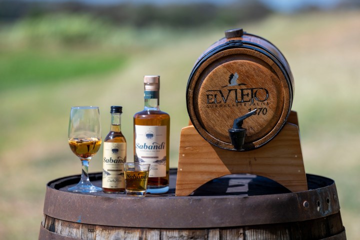 Barrel with two liquor bottles and a glass on a wooden surface outdoors.