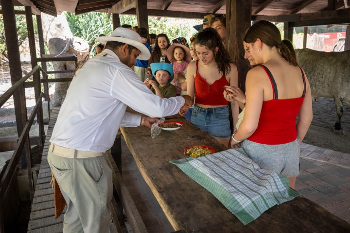 Group of people standing around a table with food outdoors.