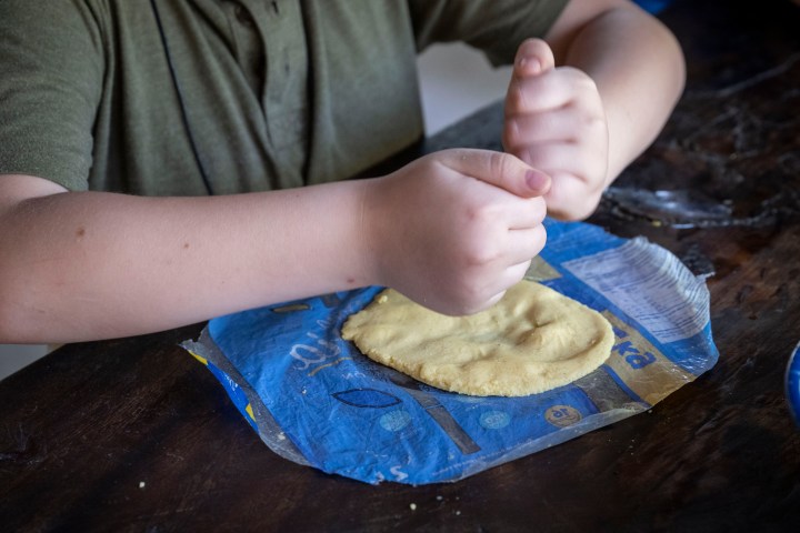 Person shaping dough on a wooden surface with hands.