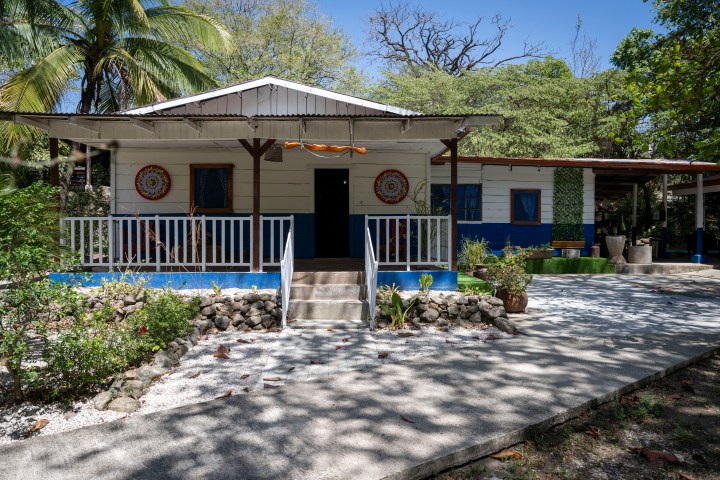 Small house with a porch, surrounded by tropical trees and plants.