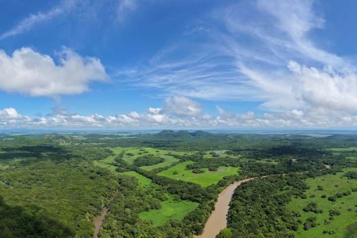 Aerial view of a river winding through lush green landscape under a blue sky with scattered clouds.