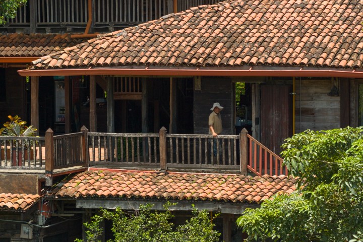 Person on wooden balcony with tiled roof and lush greenery.