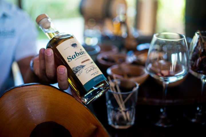 Hand holding a Saban bottle near glasses and bowls on a table.