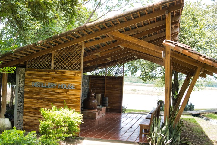Wooden distillery house with open sides, surrounded by greenery.