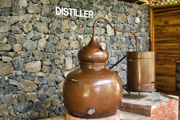 Copper distillery equipment against a stone wall labeled 'DISTILLER'.