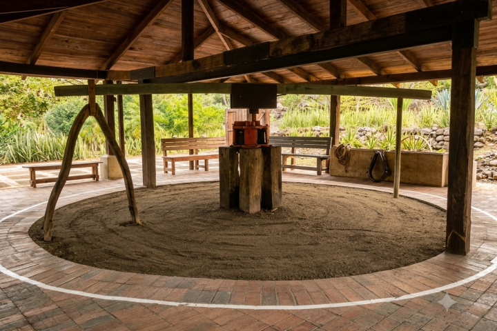 Circular wooden structure with central press and benches under a roof.