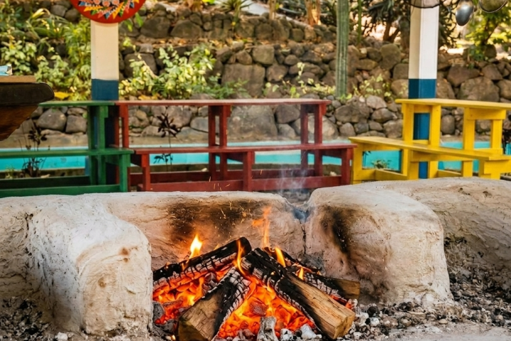 Outdoor fire pit with colorful benches and wall art in background.
