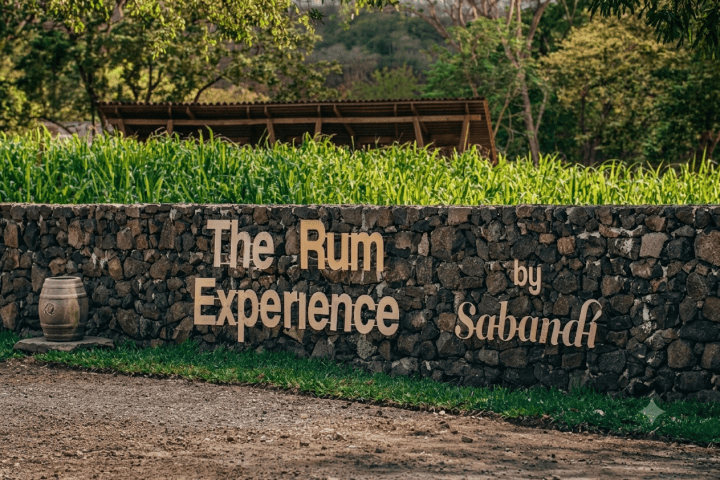 Sign reading 'The Rum Experience by Sabandi' on a stone wall with greenery behind.