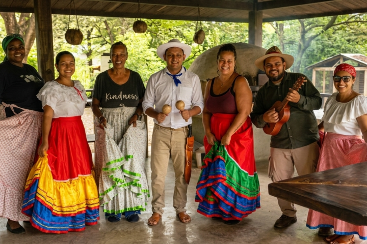 Group in colorful traditional attire posing under a pavilion.