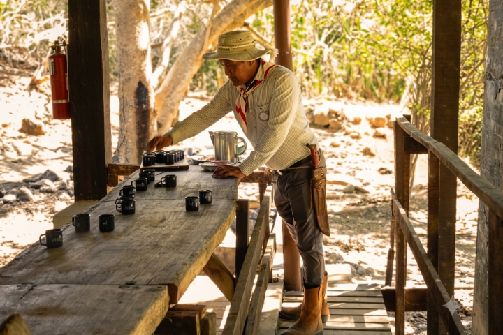 Man in cowboy hat setting up cups on a wooden table outdoors.