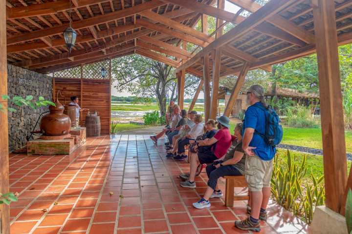 Group of people seated under wooden shelter listening to a presentation.