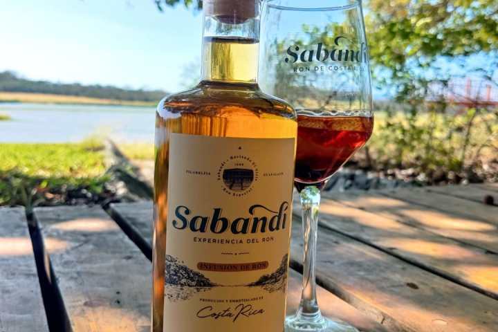 Bottle and glass of Sabandí on a wooden surface near water.