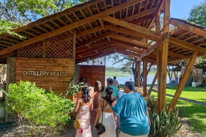 Group walking toward wooden distillery house entrance by lake.