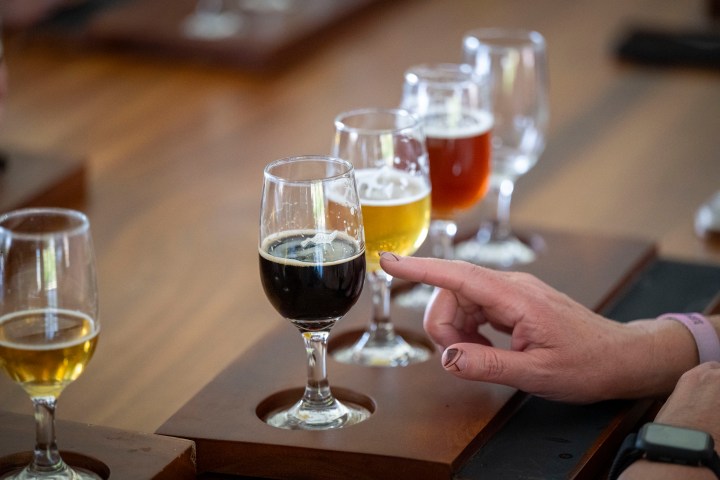 Person's hand near a flight of craft beers on a wooden table.