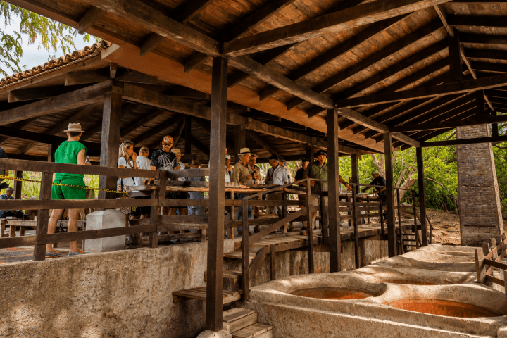 Group of people under a wooden pavilion near large basins outdoors.