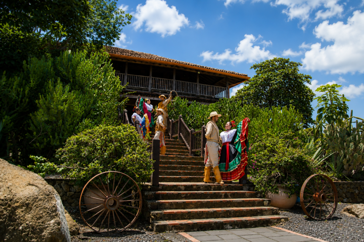 People in colorful outfits walking down stairs with greenery and a rustic building.