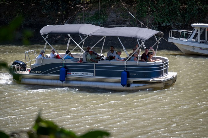 People on a pontoon boat with a canopy on a river.