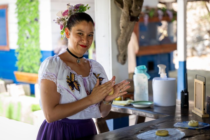 Woman in traditional dress shaping dough at an outdoor table.