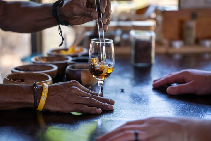 Person stirring drink in glass on table with bowls nearby.
