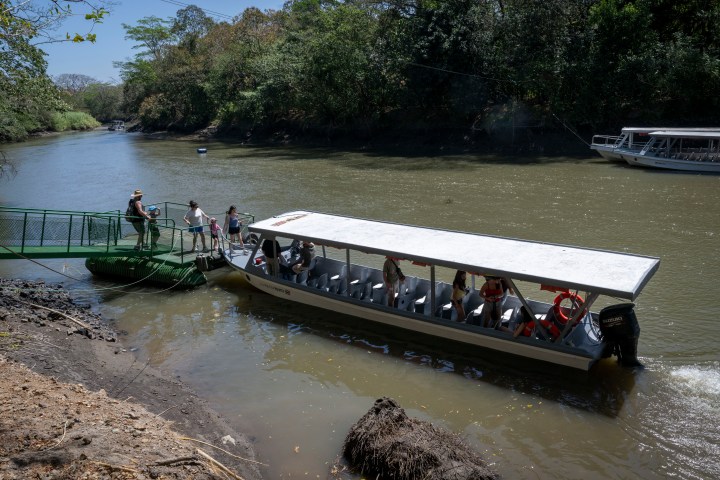 Tourists boarding a covered boat on a river at a dock.