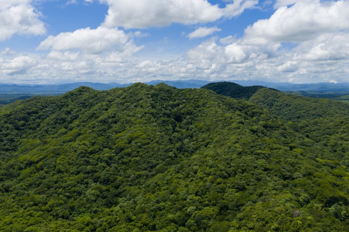 Lush green forested hills under a partly cloudy blue sky.