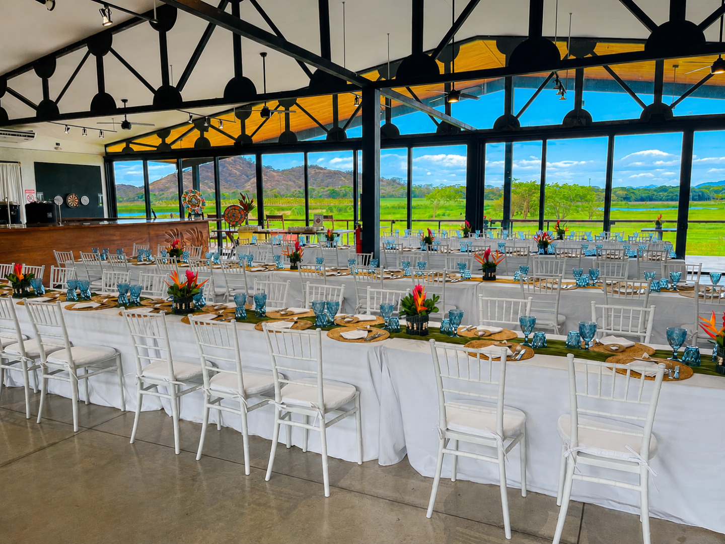 Elegant banquet hall with long tables, white chairs, and floral centerpieces overlooking scenic mountains.