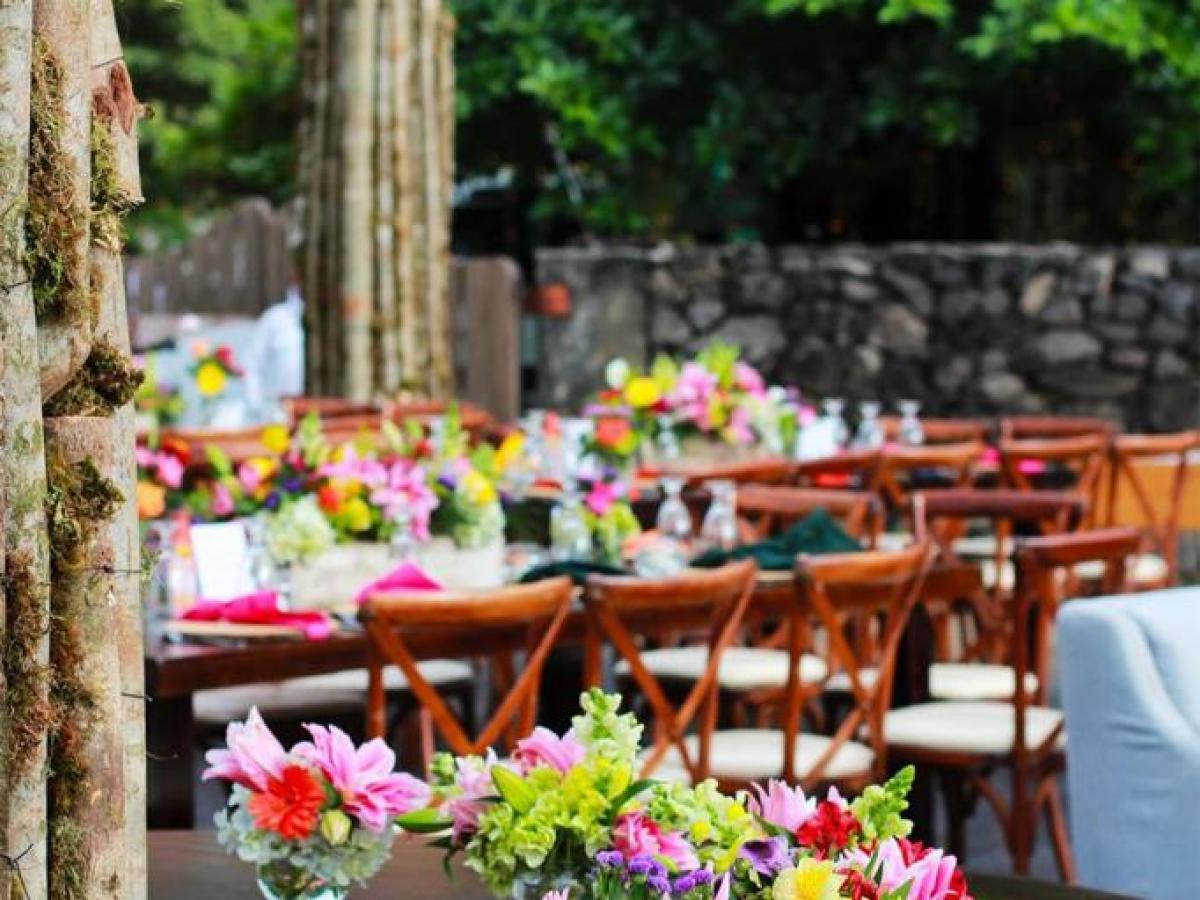 Vibrant floral arrangements on outdoor tables with wooden chairs.