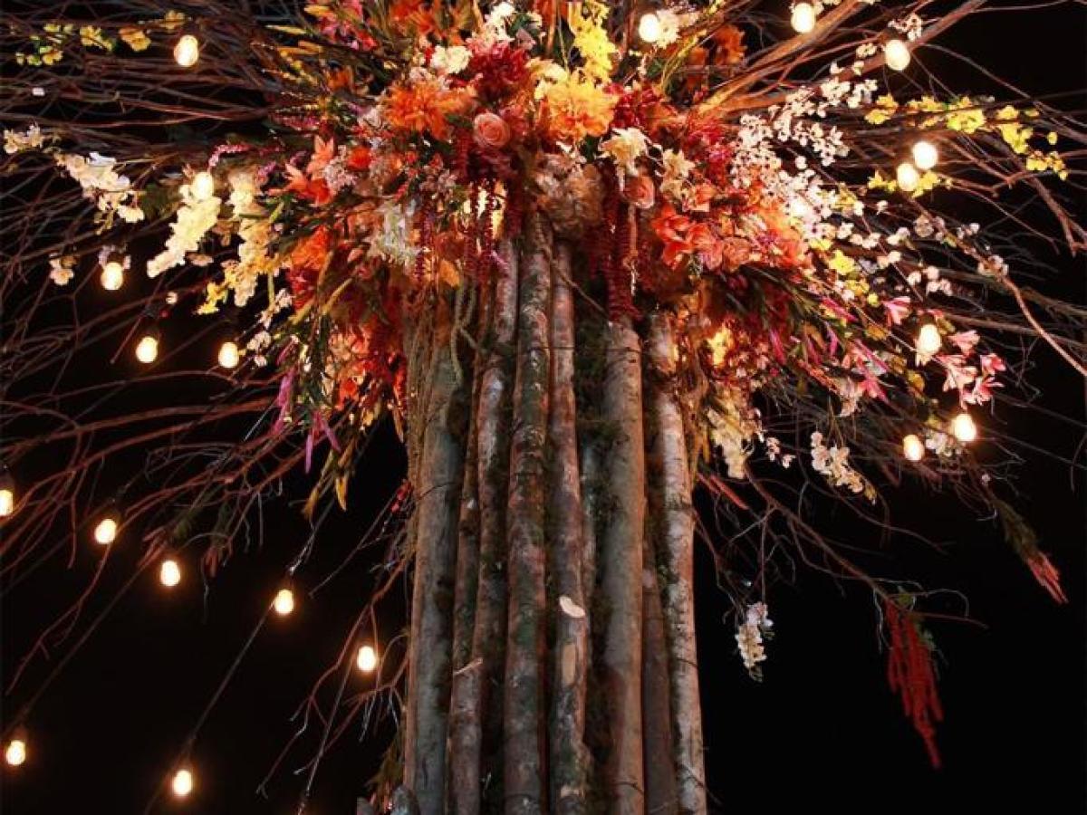 Tall tree decorated with flowers and string lights at night.