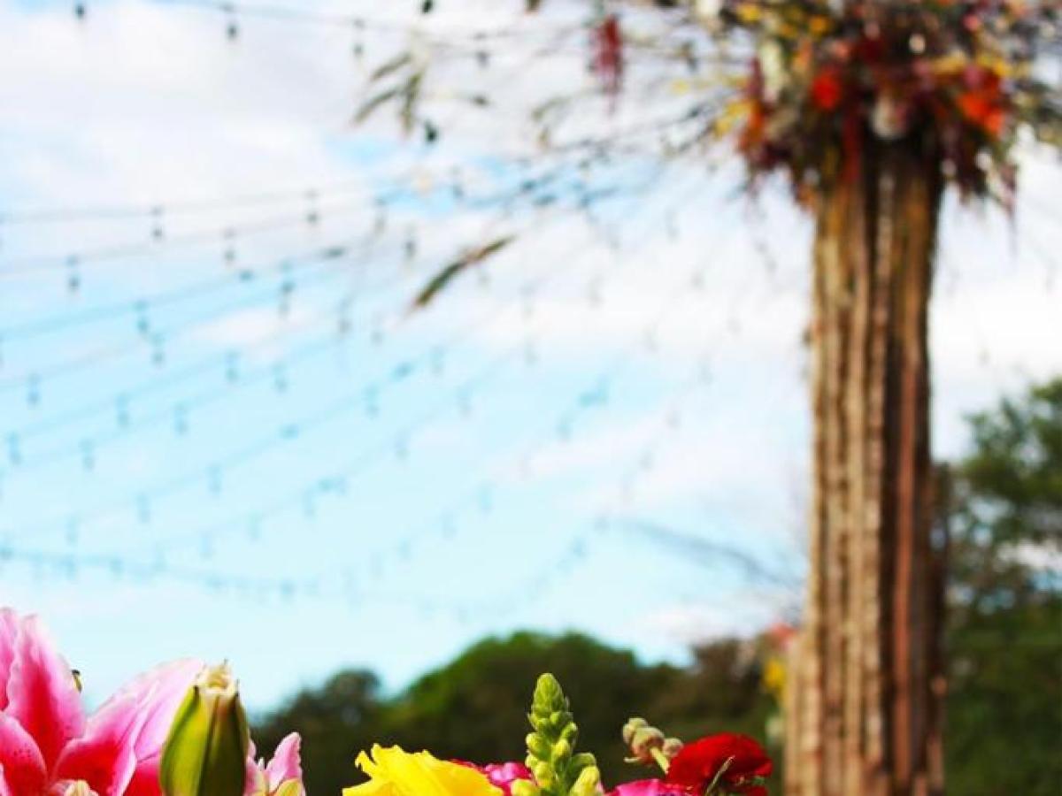 Outdoor floral arrangement with pink and yellow flowers, lights, and a tall floral structure.