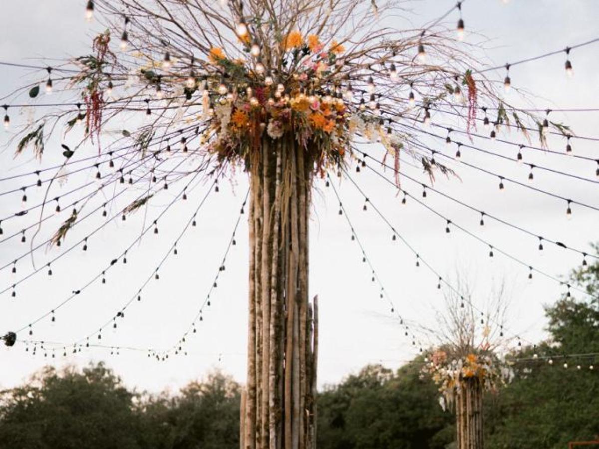 Tall centerpiece with flowers and hanging lights in an outdoor setting.