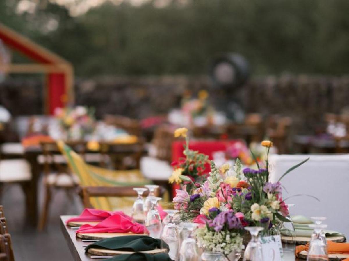 Outdoor dining table with colorful flowers, glasses, and chairs in a garden setting.