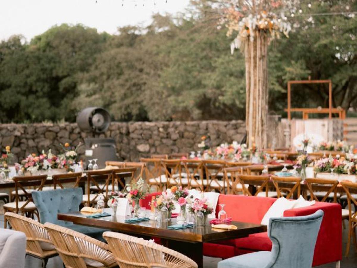 Outdoor event with tables, colorful chairs, string lights, and floral decor.