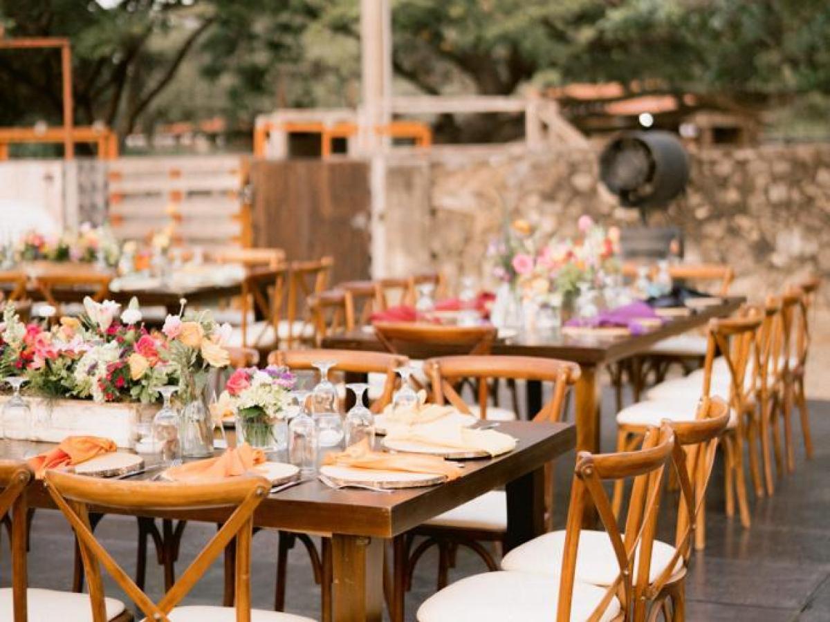 Outdoor dining setup with wooden tables, chairs, and colorful floral centerpieces.