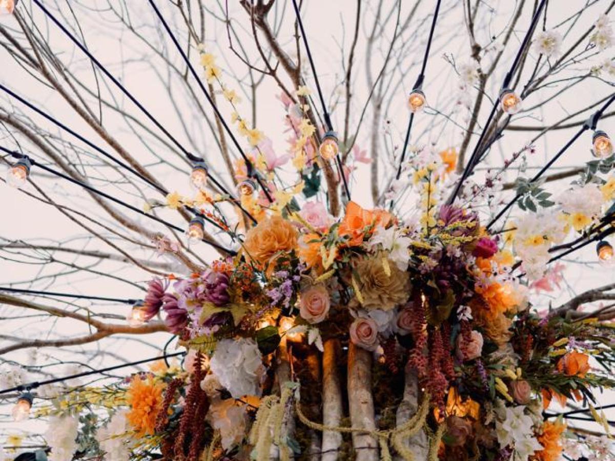 Artistic arrangement of branches with colorful flowers and string lights.