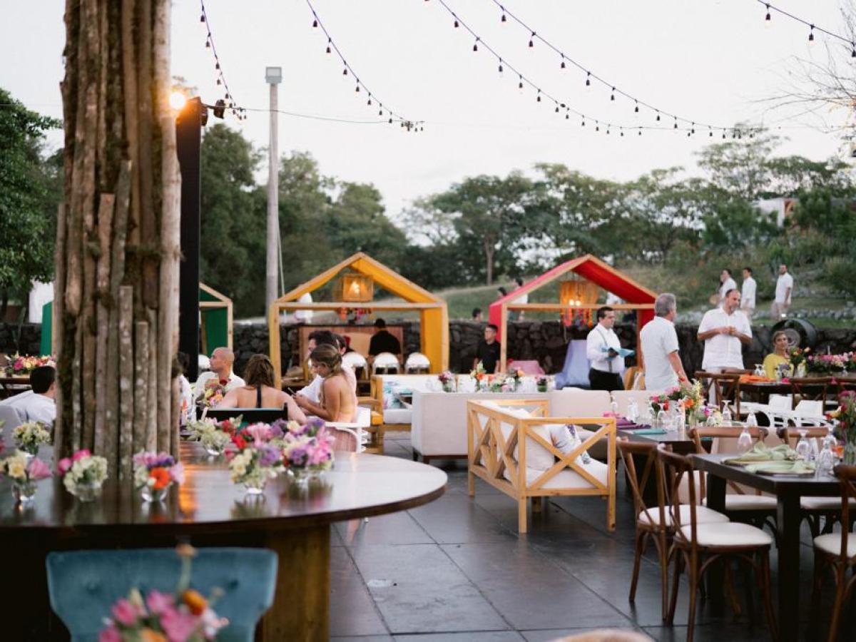 Outdoor event with tables, chairs, string lights, and small hut structures.