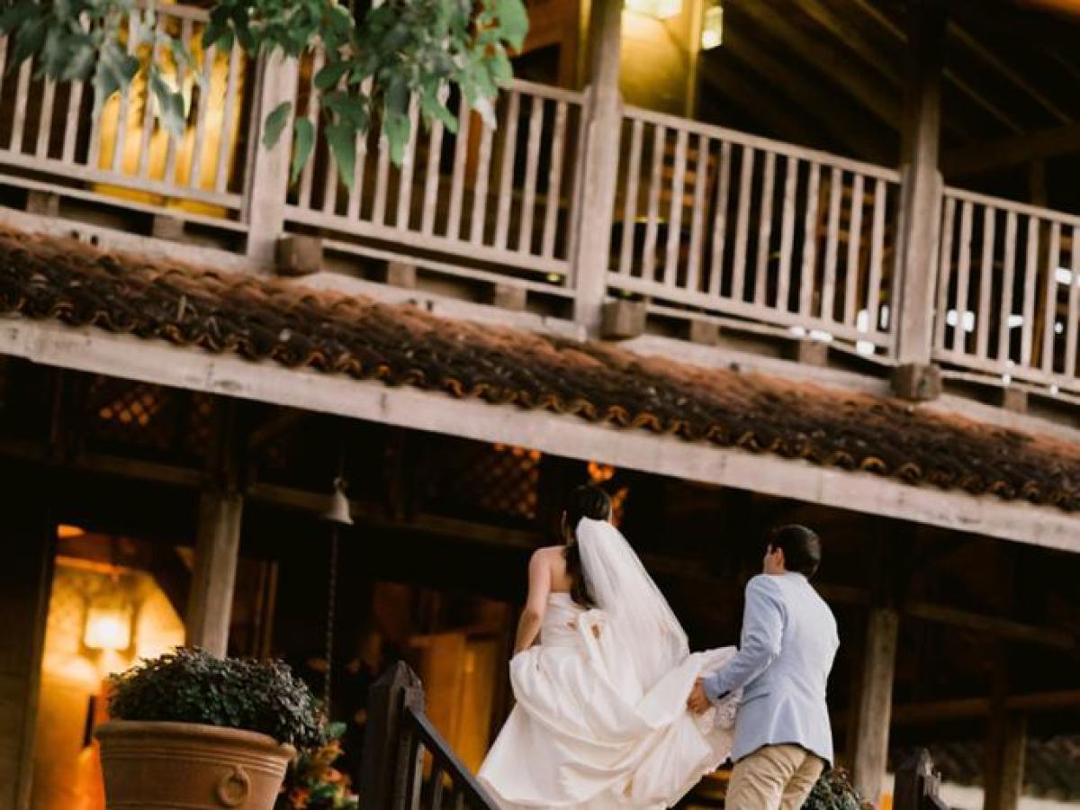 Newlyweds walking up stairs towards wooden house with balcony.