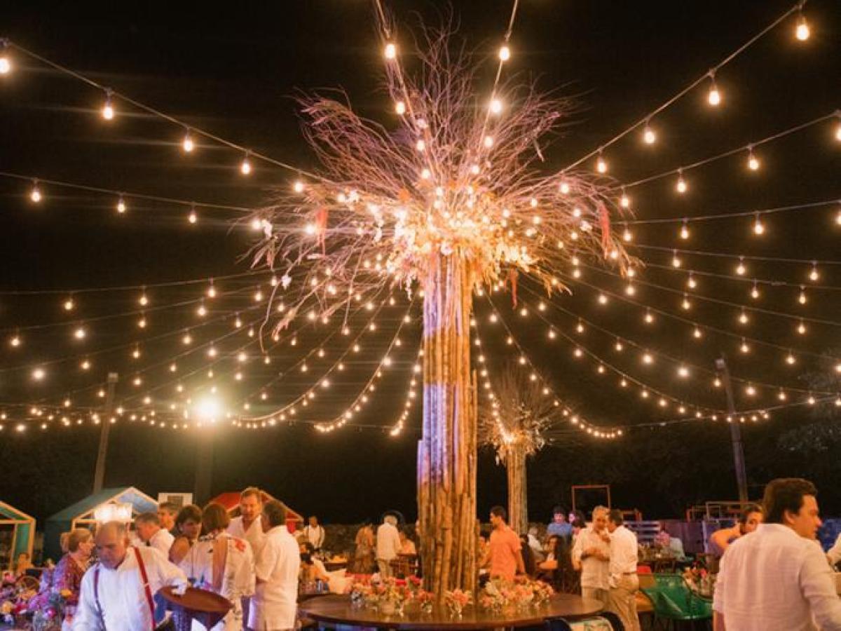 Outdoor evening party with string lights and people gathered around tables.