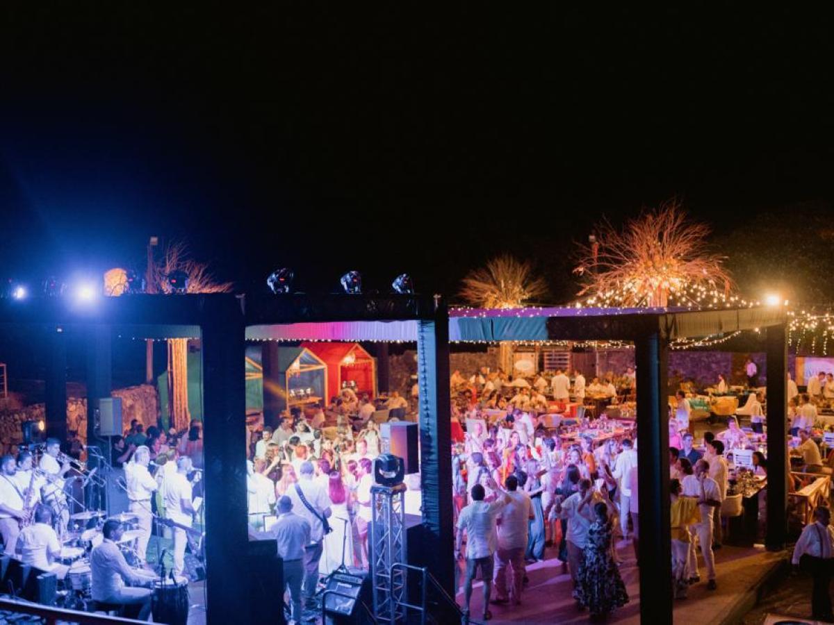 Outdoor evening wedding reception with guests dancing under string lights.